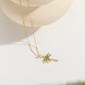 Macro shot of 14K gold plated palm tree necklace featuring green and white zircons