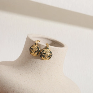 Detail view of gold textured hoop earrings with green stones on a white ceramic vase