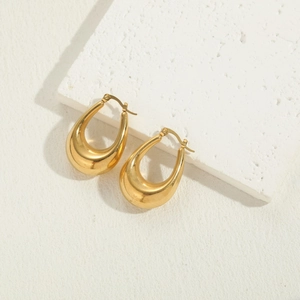 Detailed macro view of polished gold teardrop earrings resting on minimalist white stone