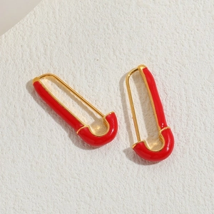 Minimalist red enamel safety pin earrings in gold finish against a beige background