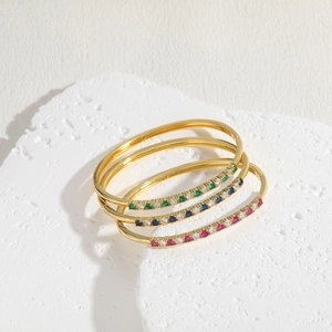 Three-piece gold-plated zircon bangles set with colorful gemstones on a white rock