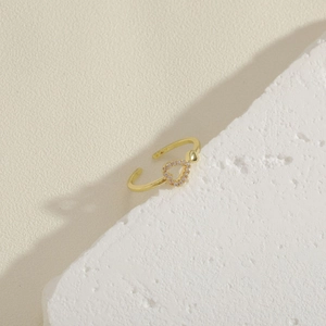 Detalle de anillo dorado con diseño de doble corazón y circonitas en soporte de piedra