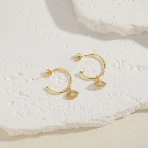 Close-up of gold evil eye earrings with opal stone on a textured stone surface