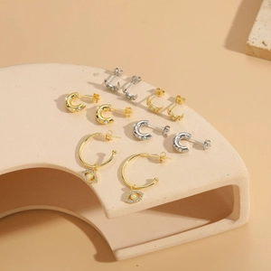 Detailed close-up of gold and silver moon opal evil eye hoop earrings on a beige pedestal