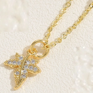 Close-up detail of leaf-shaped gold pendant with cubic zirconia inlay on fine chain
