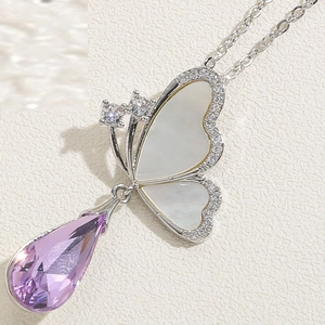Détail macro du collier papillon avec ailes en nacre et pendentif en cristal violet