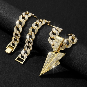 Close-up of gold iced-out Cuban link chain and paper plane pendant on black background