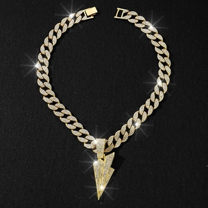 Macro view of iced out paper plane pendant with gold Cuban link chain on black background