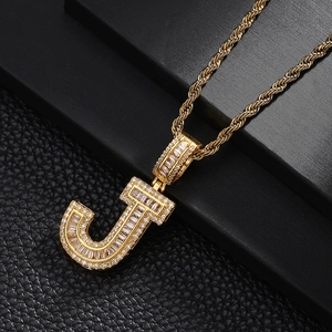 Macro shot of gold-plated J letter pendant with baguette-cut zircons on a rope chain