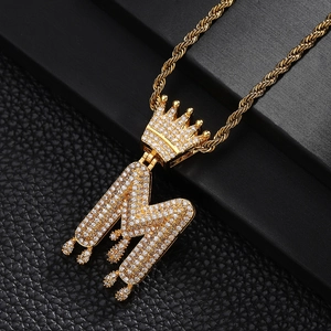 Détail macro du pendentif couronne lettre M doré glacé avec effet goutte et chaîne corde