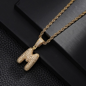 Macro detail of gold plated letter M pendant with iced out pave set cubic zirconia stones