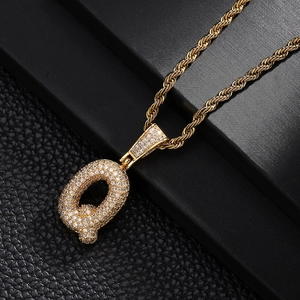Macro shot of iced out bubble letter Q pendant with gold rope chain and zircon stones