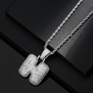 Macro detail of iced-out bubble letter H pendant with silver rope chain for hip hop style