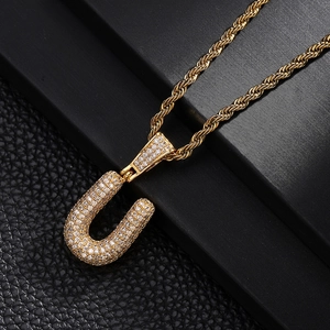 Macro detail of gold U-letter pendant with pavé zircons and elegant rope chain