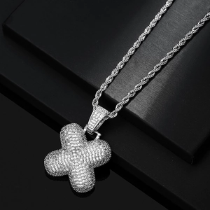 Macro view of iced out silver X-shaped pendant with cubic zirconia and rope chain