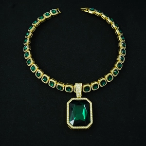 Macro shot of Cuban chain with emerald cut green gemstones set in golden metal settings