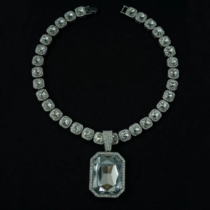 Detail of silver cuban chain necklace featuring a large square crystal pendant on black backdrop