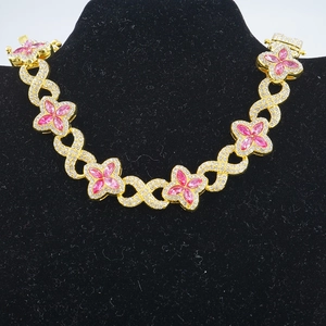 Dettaglio della collana dorata a maglie infinito con ciondolo a trifoglio rosa e zirconi