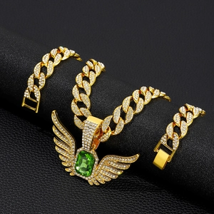 Detailopname van hiphop vleugel hanger met groene edelsteen en witte strass op gouden ketting