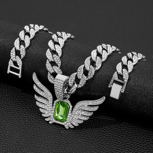Detail van zilveren iced-out cubaanse ketting en engelenvleugel hanger met groene steen