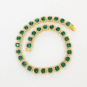 Macro view of iced out hip hop necklace with emerald cut green stones and gold plating