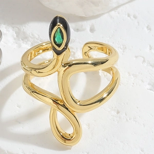 Snake shaped gold ring with black enamel and green gemstone on textured white stone