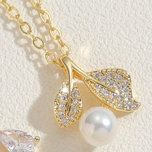 Détail macro du collier cerise dorée avec feuilles de zircon et perle nacrée