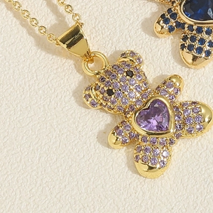 Macro shot of a gold-plated bear pendant with purple heart gem and pave set crystals