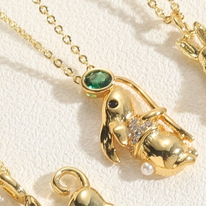Macro shot of gold rabbit pendant with green stone and pearl on elegant necklace