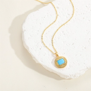 Detail of a round gold pendant with a square blue zircon on a white textured stone