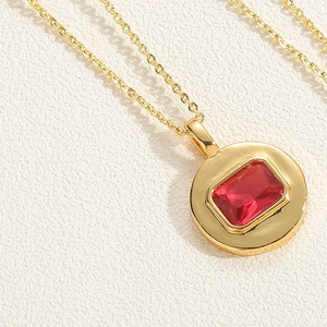 Close-up of golden round pendant with rectangular red zircon on white leather texture