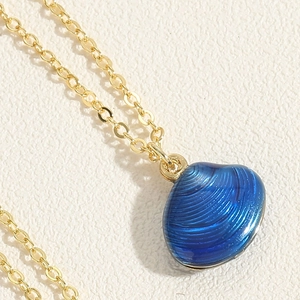 Macro-opname van een blauwe schelphanger met gouden ketting op witte ondergrond