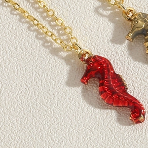 Macro view of gold seahorse necklace with vibrant red enamel detail on a white surface