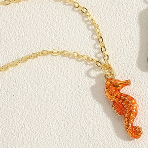 Detailed macro shot of the orange enamel seahorse pendant and its gold-plated chain