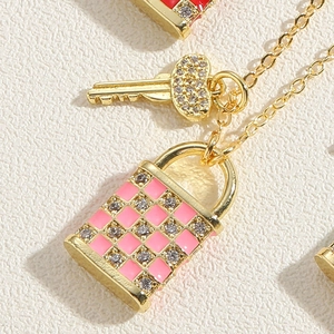 Vue macro du pendentif clé dorée et serrure à damier en émail rose avec zircons