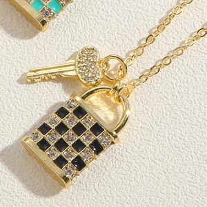 Détail macro du collier avec pendentif cadenas à damier doré et petite clé sertie
