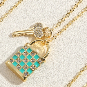 Détail macro du collier en or avec cadenas en émail vert damier et clé en cœur cristal