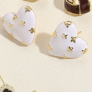 Makroaufnahme weißer Emaille-Herzohrstecker mit goldenen Blumendetails und Metallstiften