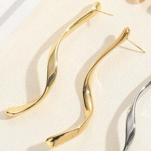 Close-up of polished gold wavy earrings with 925 silver needles on a textured background