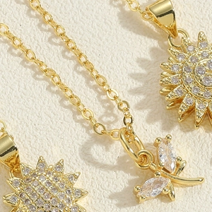Detail van draaiende zonnebloem- en libelhangers met zirkonia op gouden ketting