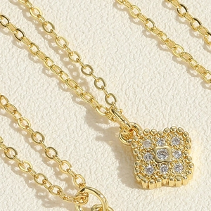 Dettaglio macro della collana con ciondolo a quadrifoglio dorato e zirconi su carta ruvida