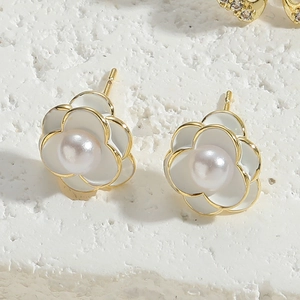 Macro shot of white enamel flower earrings with central pearl on a stone background