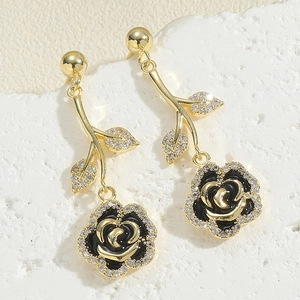Close-up of gold rose earrings featuring black enamel petals and sparkling white zircons