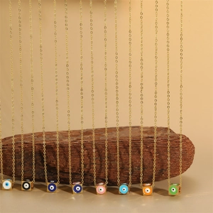 Gold cube evil eye pendant necklace with colorful enamel charms on rustic wood stand