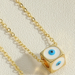 Macro shot of gold cube pendant with enamel evil eye designs and fine cross chain