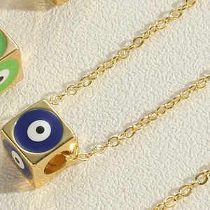 Macro shot of gold dice pendant with blue and green evil eye enamel on link chain
