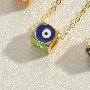 Macro view of golden cube evil eye pendant with colorful enamel eyes and polished finish
