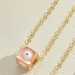 Macro shot of gold cube pendant featuring pink enamel evil eye charms on link chain
