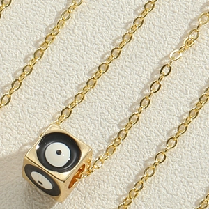 Detail of gold cube pendant with evil eye pattern on a fine chain necklace