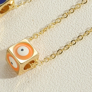 Macro shot of gold cube pendant necklace with orange and white evil eye pattern